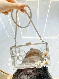 Detail of transparent acrylic clutch bag with 3D floral accents and rhinestone chain