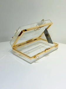 Detailed view of clear acrylic clutch with white 3D flowers and gold metal hardware