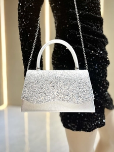 Detail of silver glitter evening clutch with metal handle and chain over a black dress
