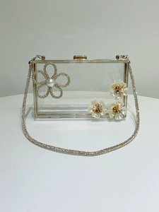 Detail of transparent acrylic clutch bag featuring rhinestone flowers and pearl center