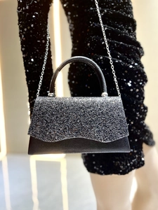 Detail of sparkly black evening bag with wavy flap, round handle and silver chain strap