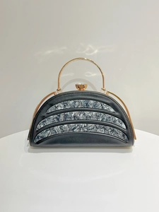 Detail of semicircular black evening clutch with marble texture and gold ring handle