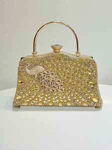 Close-up of golden evening clutch featuring crystal peacock design and round metal handle
