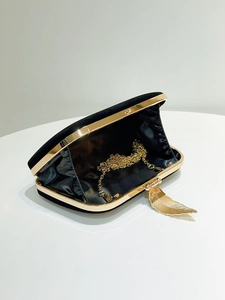 Detail of black velvet evening bag featuring gold feather clasp and metal chain strap