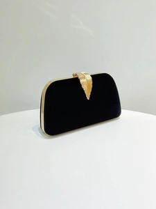 Detail of elegant black velvet evening clutch with gold leaf-shaped metal clasp