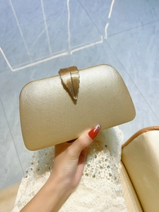 Detail of gold evening clutch with textured matte metal finish and leaf-patterned clasp