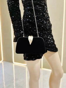 Detail of black velvet evening clutch featuring a gold leaf clasp and metal chain strap