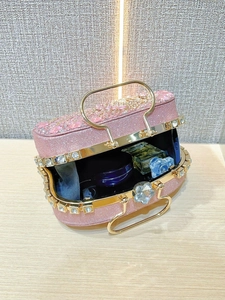 Detalle del interior de un bolso de fiesta rosa con pedrería y varios cosméticos