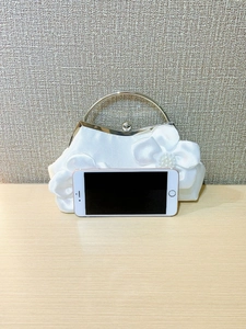 Detailed scale view of a white satin evening bag with a pearl bow and metal ring handle