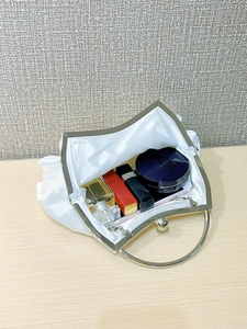 Spacious interior of white satin evening clutch holding perfume, lipstick and phone