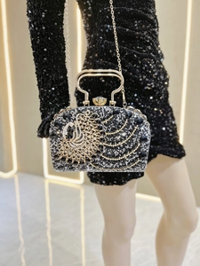 Detalle de bolso de noche negro con ala de pavo real dorada y cristales brillantes