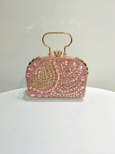 Detalle del patrón de pluma de pavo real dorado y cristales rosas en el bolso de noche