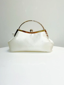 Detail of white satin evening bag featuring gold circular handle and vintage clasp