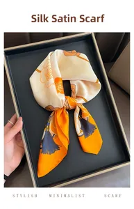Detailed view of folded camellia floral satin square scarf with orange borders in black tray