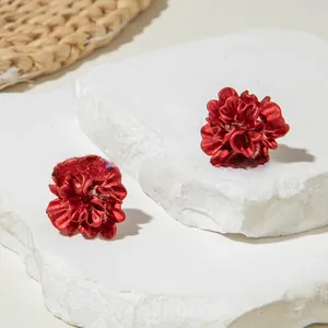 Macro shot of matte red 3D flower stud earrings on white stone and straw background