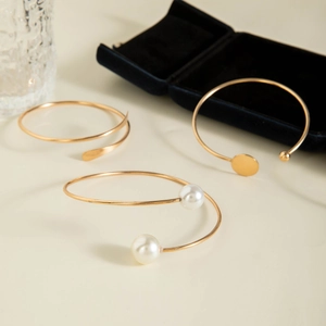 Three-piece gold bangle set with faux pearls and metal discs on a beige surface