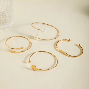 Detailed view of four minimalist gold-plated open bangles with pearls and disk accents