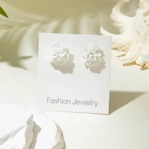 Detailed macro view of 3D white floral resin earrings on a fashion display card