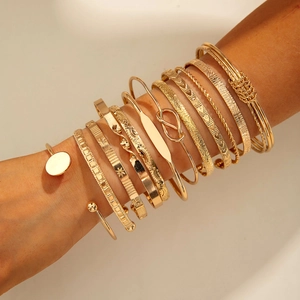 Set of 12 stackable gold bracelets featuring twisted bands and pearl accents on a model