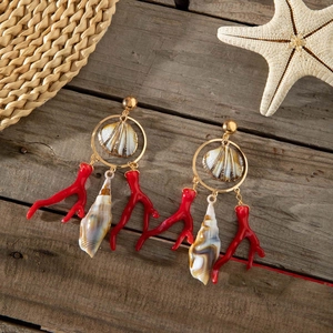 Detalle de pendientes de aro dorados con concha natural y colgantes de coral rojo