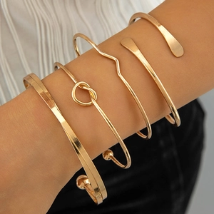 Detail of four gold-plated minimalist bangles styled on a wrist for layered fashion