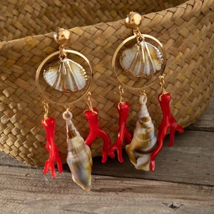 Detalle de pendientes de coral con concha natural y aros dorados en cesta de paja