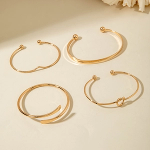 Detail of four-piece gold metal bracelet set featuring minimalist cuffs and knotted designs