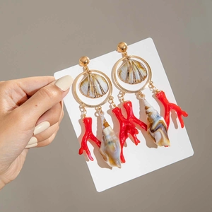 Detalle de pendientes marinos con ramas de coral rojo y dijes de conchas doradas elegantes