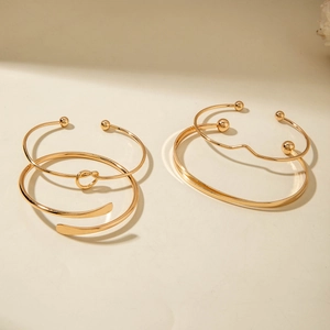 Detailed close-up of a four-piece gold stackable bracelet set with pearl and knot accents