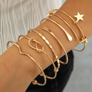 Detail of five-piece gold bangle set with star charms and textured bangles on model wrist