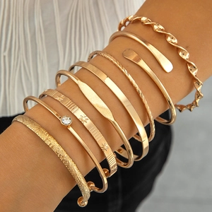Close-up of stacked gold alloy bracelets with star relief and pearl accents on wrist