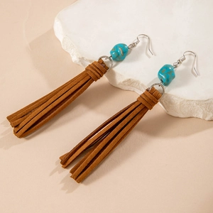 Detalle de pendientes bohemios con flecos y cuentas turquesas sobre piedra blanca
