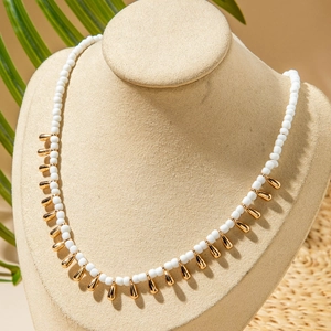 Détail de collier en perles blanches avec pendentifs gouttes dorées sur buste beige