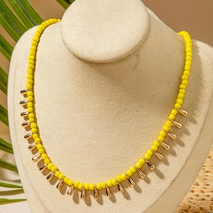 Collier de perles jaunes bohème avec pendentifs dorés en goutte sur buste beige