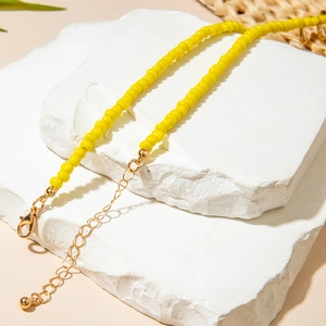 Détail d'un collier de perles jaunes avec fermoir mousqueton doré sur pierre blanche