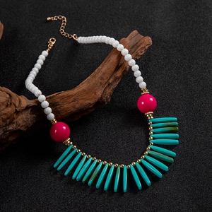 Détail d'un collier bohème avec perles roses en résine et franges turquoise sur bois