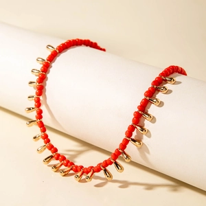Détail du collier de perles rouges bohème avec pendentifs dorés sur support blanc