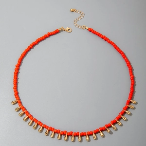 Détail d'un collier bohème en perles rouges avec des pendentifs gouttes dorés élégants