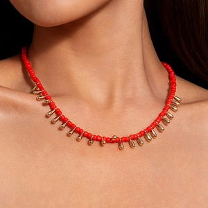 Détail du collier de perles rouges avec pendentifs gouttes dorés sur le mannequin