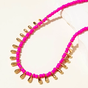 Détail d'un collier bohème en perles fuchsia avec des breloques dorées en forme de goutte