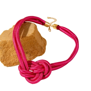 Collier à nœuds tressés magenta avec fermoir doré posé sur des pierres naturelles