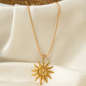 Détail macro du pendentif soleil doré avec centre en spirale sur fond de soie beige