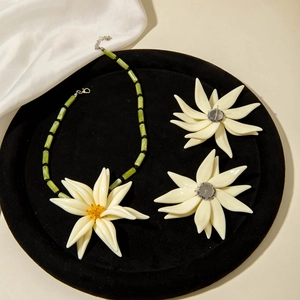 Détail d'un ensemble de bijoux en résine avec fleurs blanches et collier de perles vertes