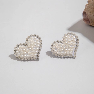 Détail de boucles d'oreilles en forme de cœur avec perles blanches et strass brillants