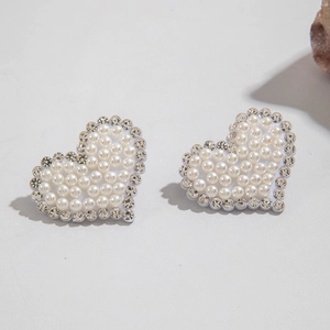 Gros plan de boucles d'oreilles cœur en perles et strass brillants sur fond gris chic