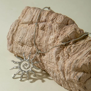 Vue détaillée du pendentif soleil argenté avec spirale et chaîne à billes sur roche