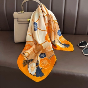 Elegant floral silk scarf in orange and beige draped on a stylish beige handbag