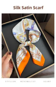 Détail d'un foulard en satin soyeux avec motif chaîne dorée et bordure orange vif