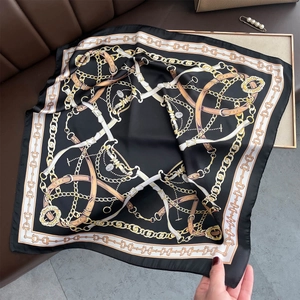 Détail d'un foulard en soie satinée avec motifs de chaînes dorées sur fond noir chic