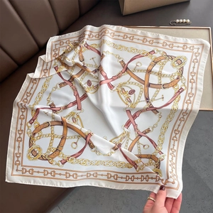 Détail d'un foulard carré en soie avec motif chaîne dorée et bride sur fond crème